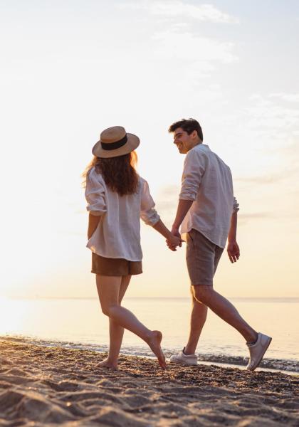 Coppia che cammina sulla spiaggia al tramonto, mano nella mano.