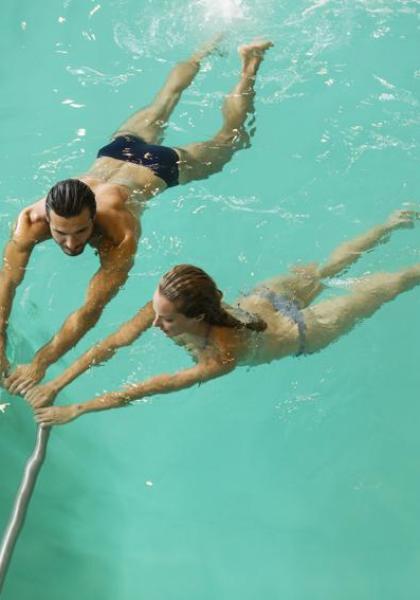 Due persone nuotano in piscina, tenendosi al corrimano.