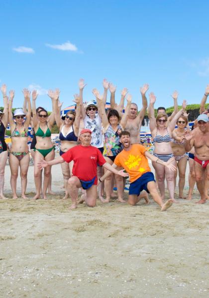 Gruppo di persone in spiaggia con braccia alzate.