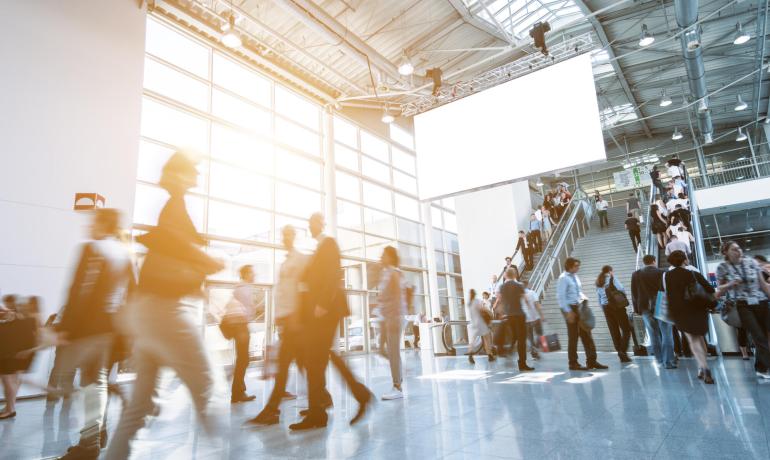 Persone camminano in un moderno centro conferenze con grandi finestre.