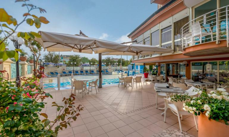 Terrazza con piscina, sedie e ombrelloni in un ambiente soleggiato.