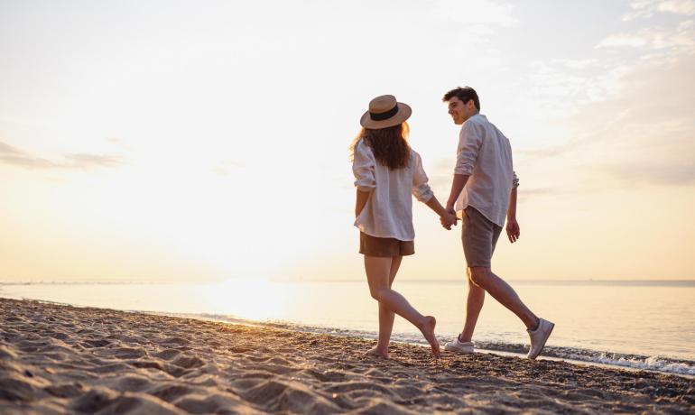 Coppia che cammina sulla spiaggia al tramonto, mano nella mano.