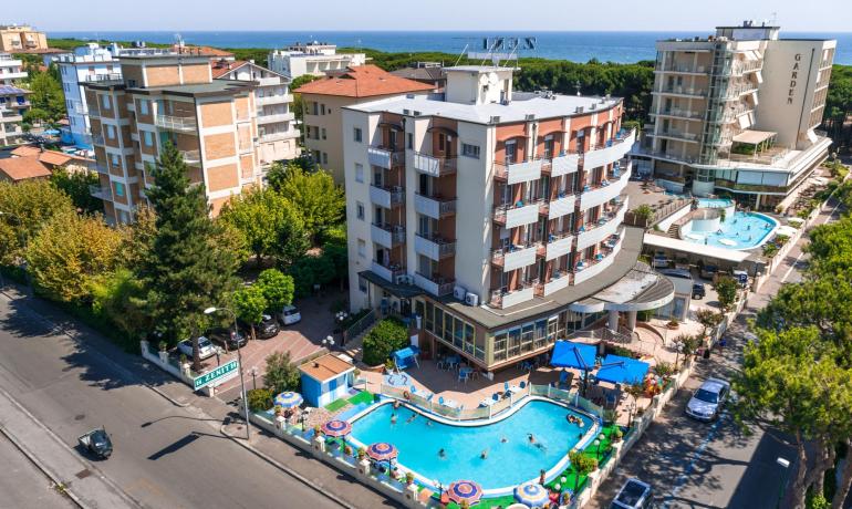 Hôtel avec piscine près de la mer, entouré de bâtiments et de végétation.