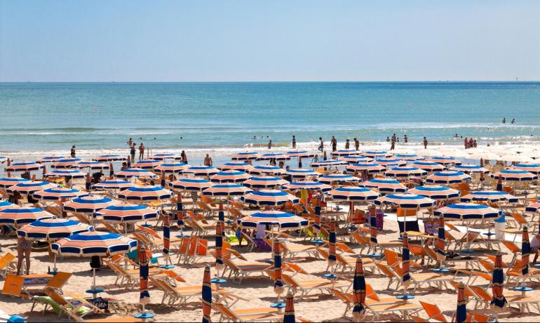 Crowded beach with umbrellas and people swimming in the sea.