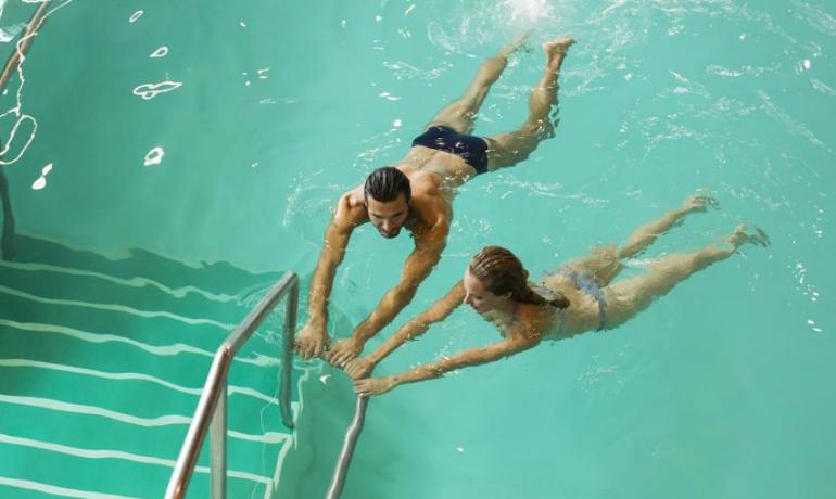 Due persone nuotano in piscina, tenendosi al corrimano.