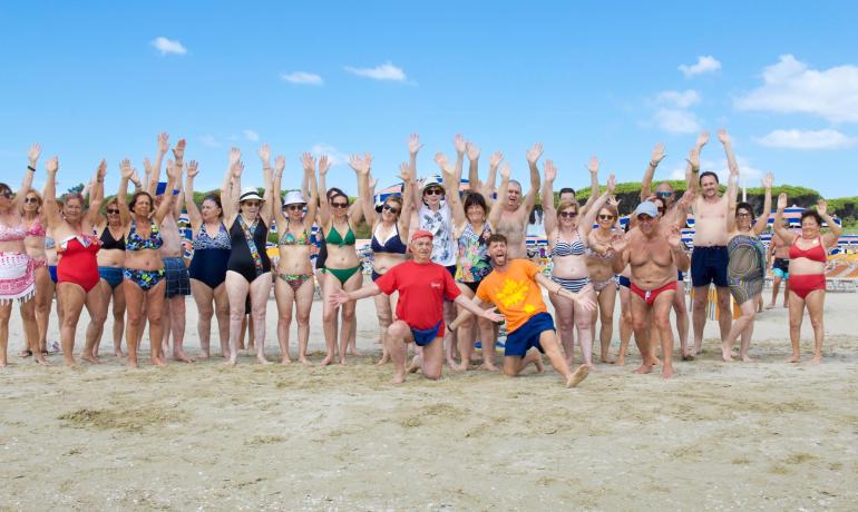 Gruppo di persone in spiaggia con braccia alzate.